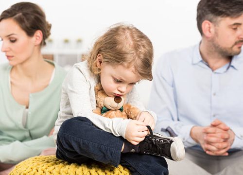 Photo of a gloomy young family with a sad little bou hugging a teddy bear, and his parents with depressed looks